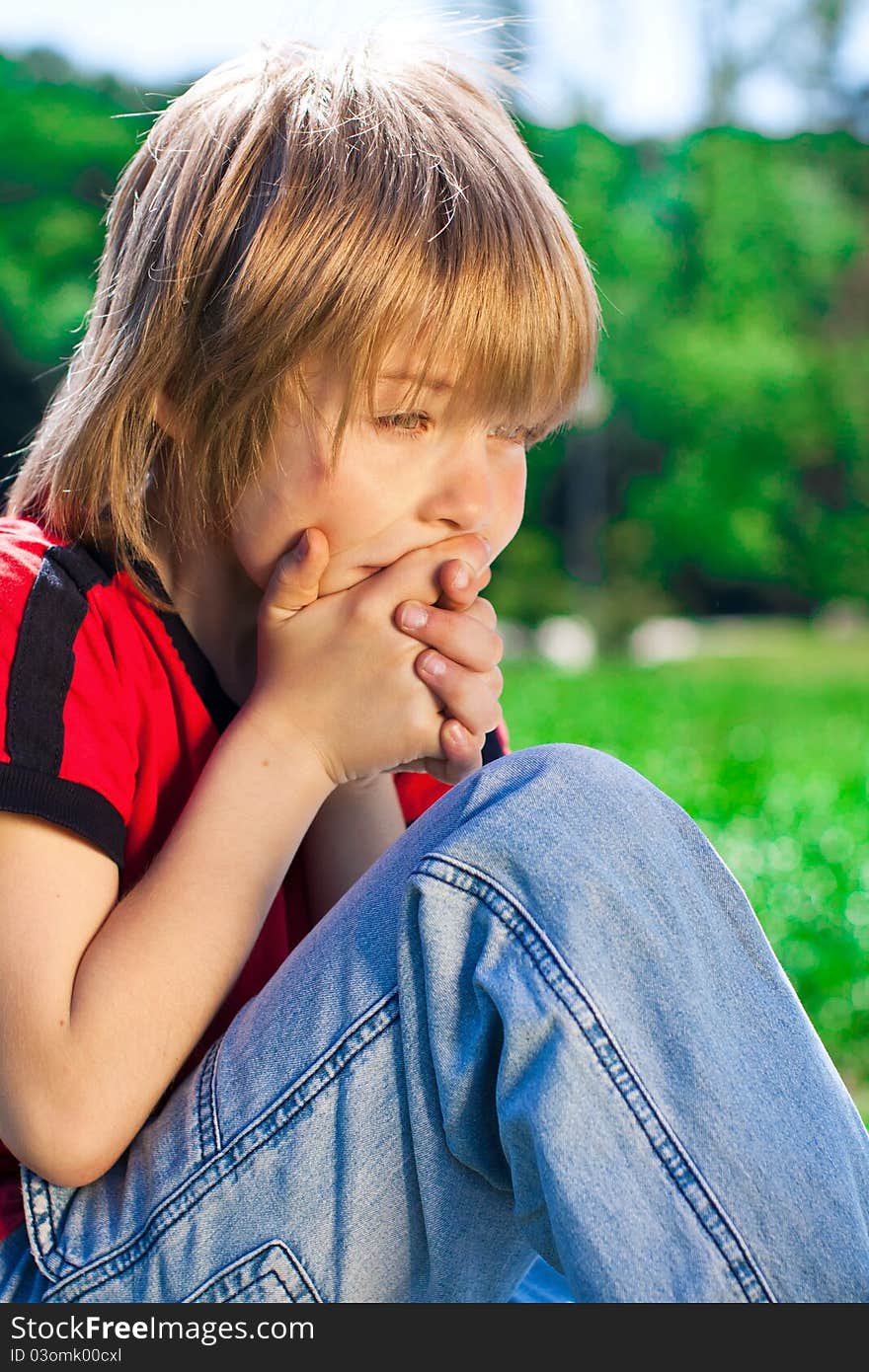 The boy with thoughtful look is sitting at the park