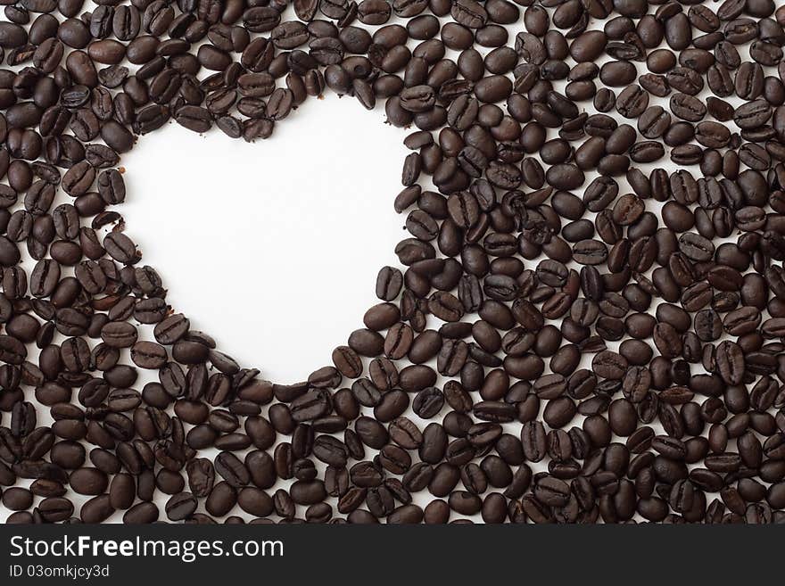 Whole espresso coffee beans spread out on a white surface with a heart-shaped hole. Whole espresso coffee beans spread out on a white surface with a heart-shaped hole.