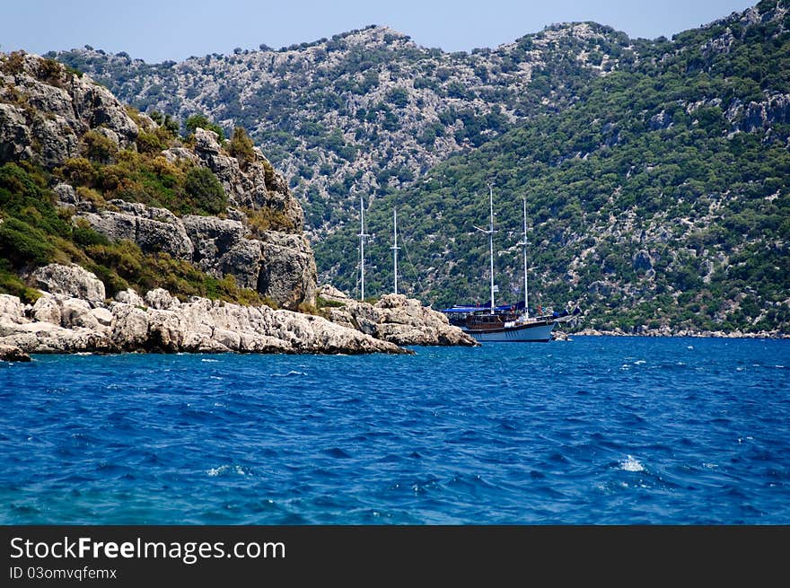 The yacht in harbor among rocks and blue sea