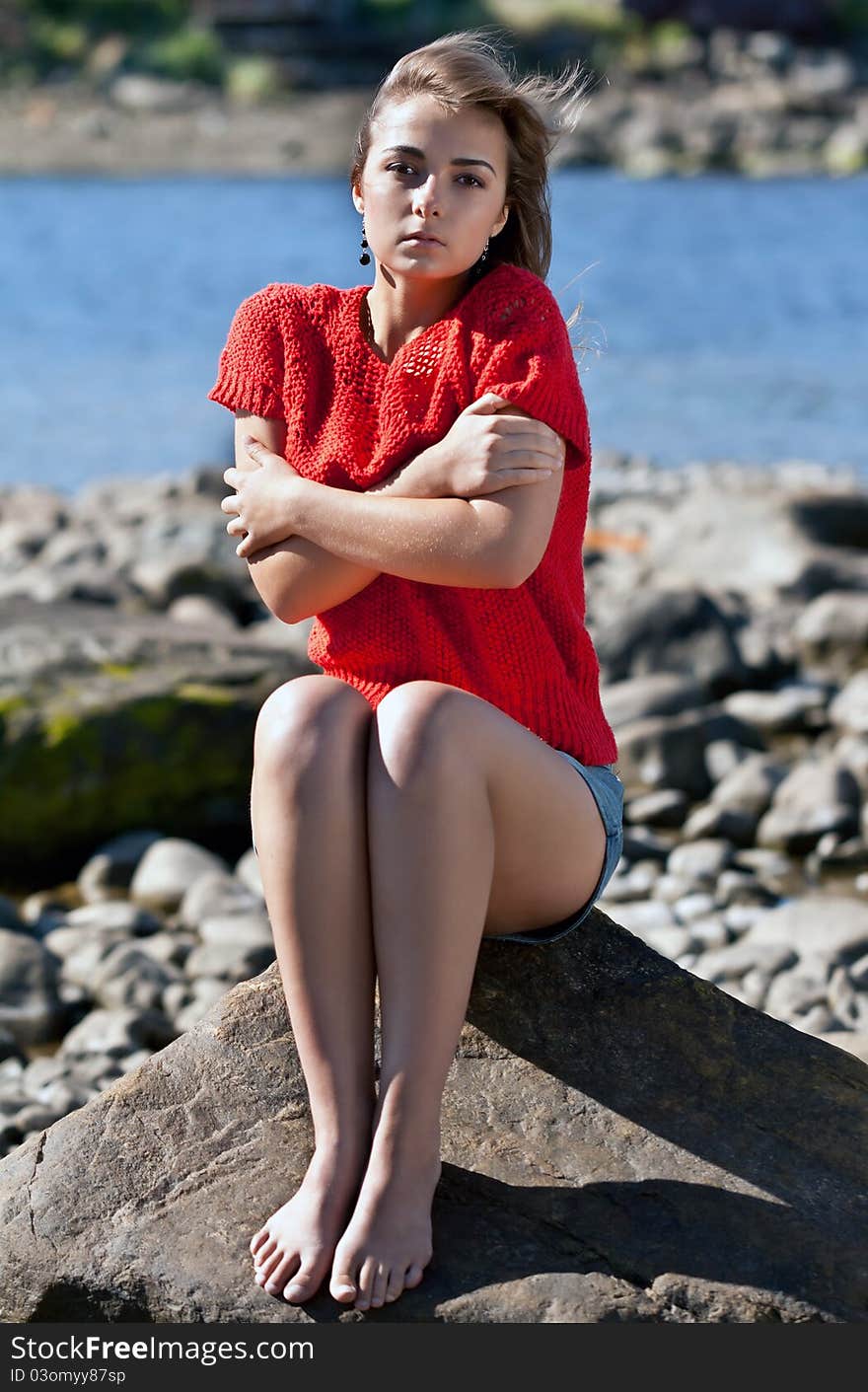 Girl badly frozen sitting on a rock in a red sweater against the rocky shore of the White Sea