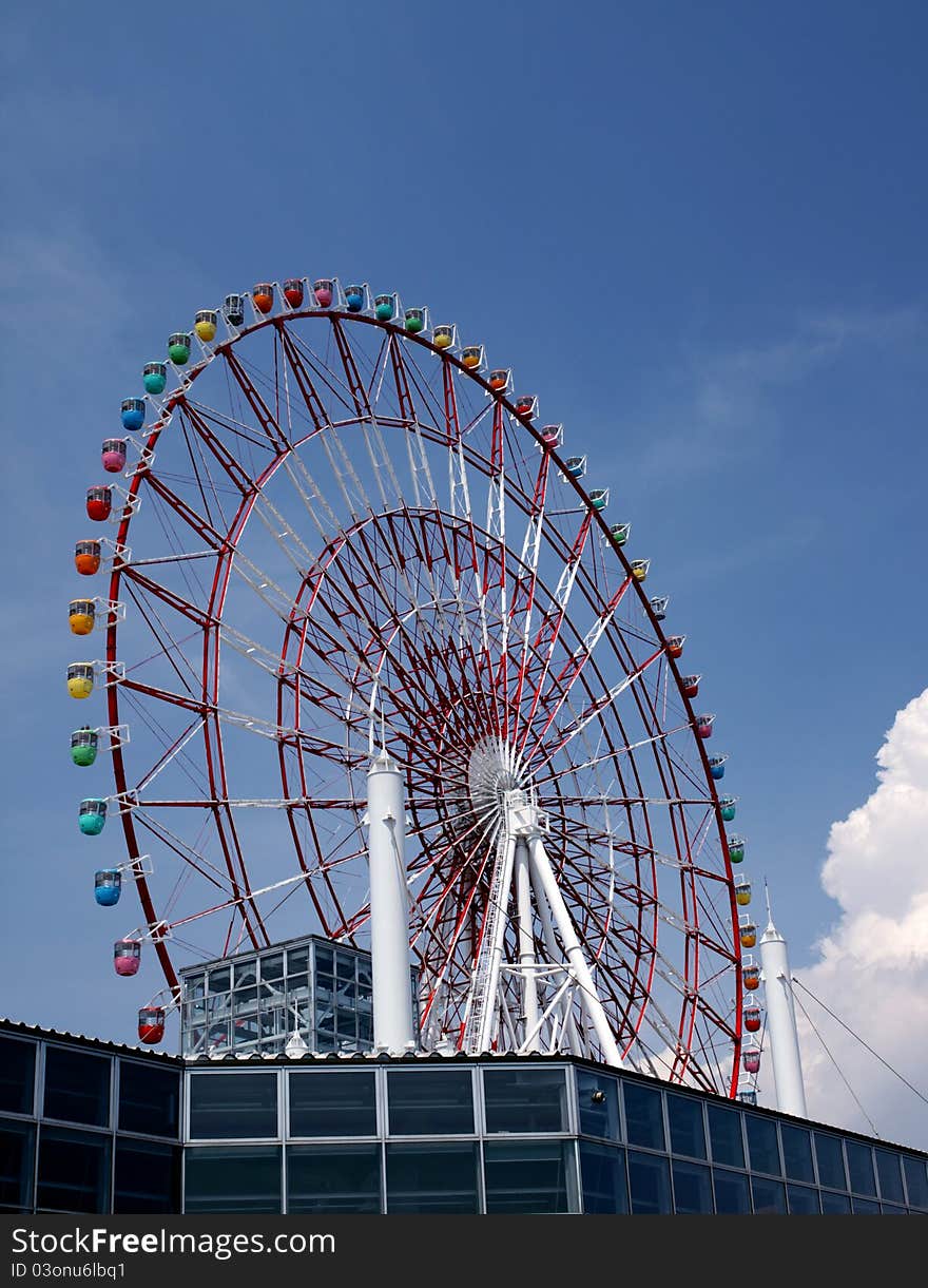 Low angle view of ferris wheel with colorful gondolas and blue sky background.