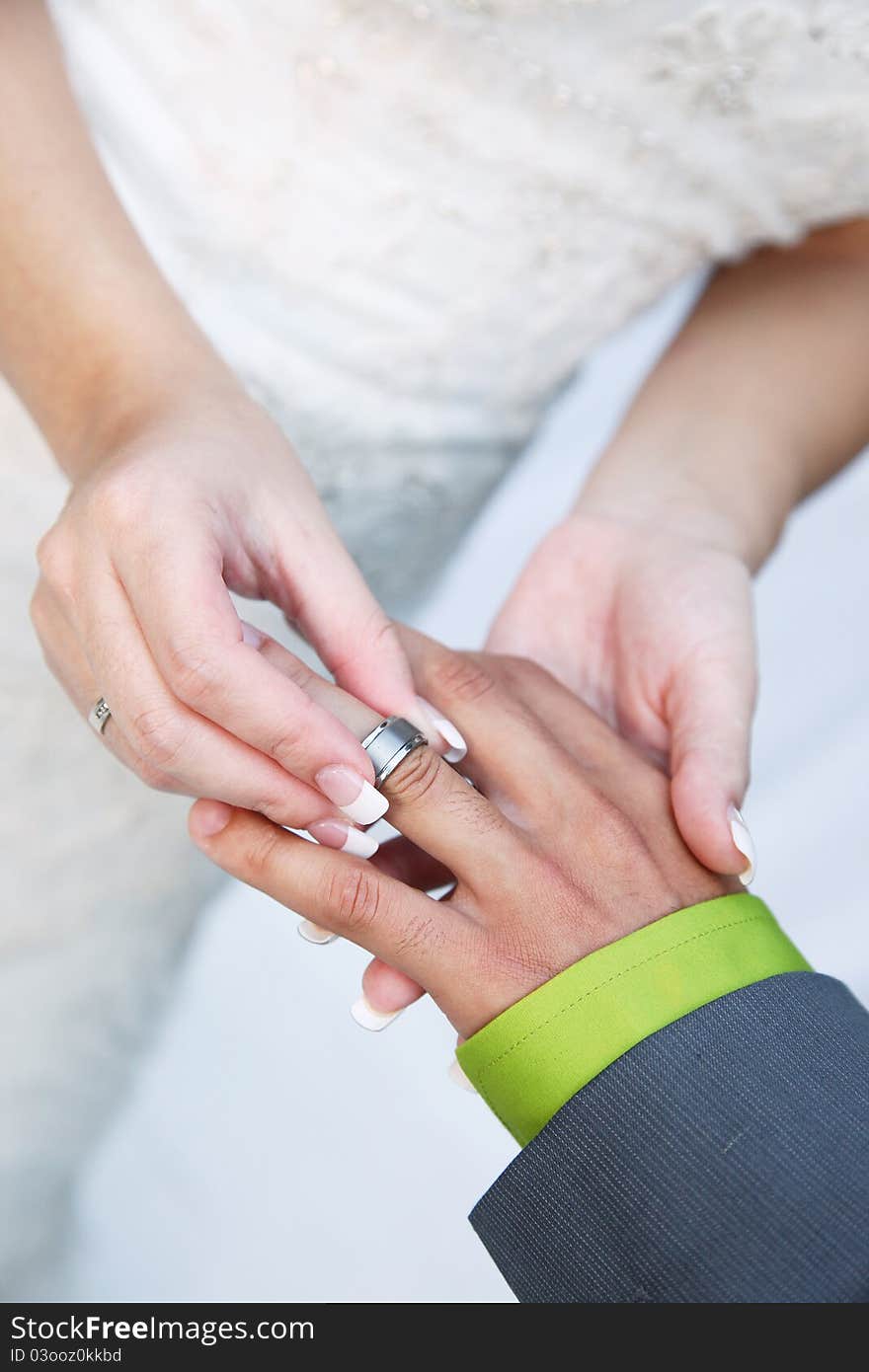 Husband and wife's hands with wedding ring. Bride puts silver band on grooms finger. Brides wedding dress in background. Husband and wife's hands with wedding ring. Bride puts silver band on grooms finger. Brides wedding dress in background.