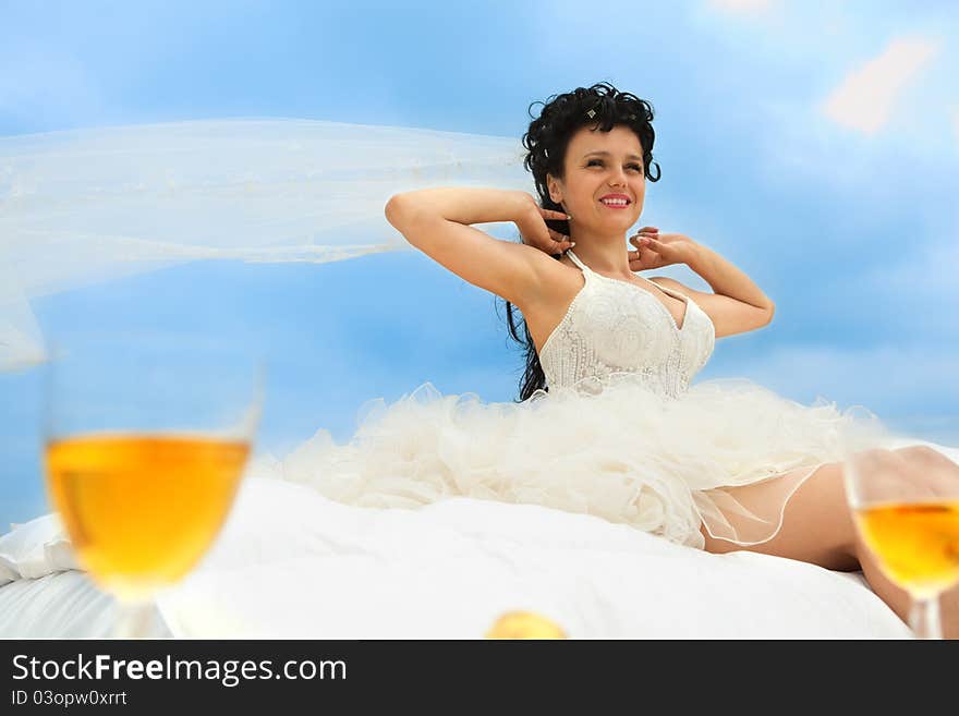 Young bride in bed at the coastline against cloudy sky