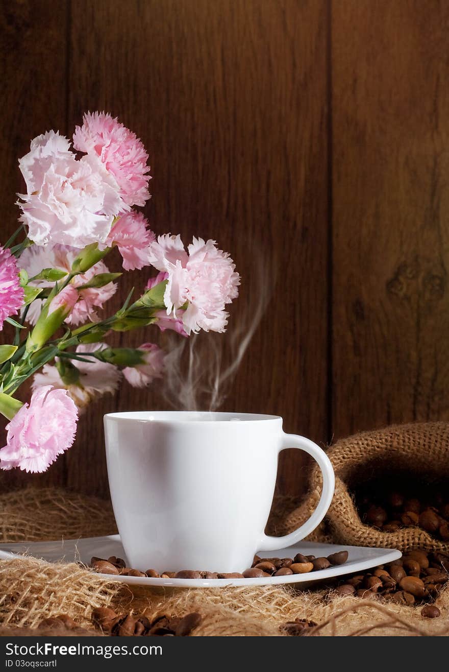 Cup and coffee beans and flowers on dark background.