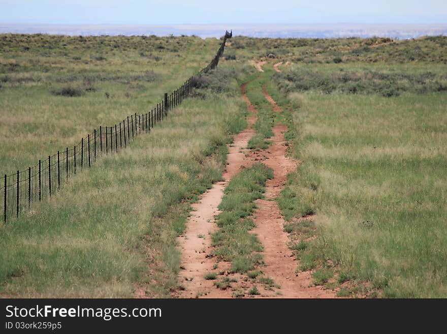 A back country road fades into the horizon along a barbed wire fence.