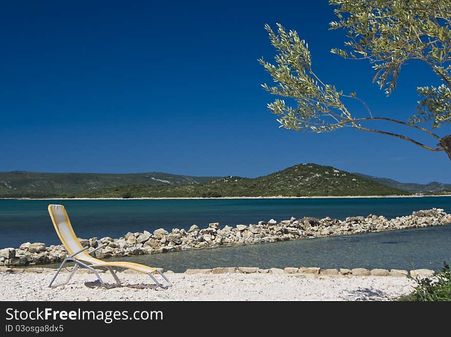 Olive tree and deck chair on the coastline of Turanj with the blue sea and islands. Olive tree and deck chair on the coastline of Turanj with the blue sea and islands