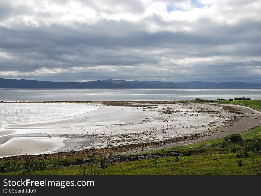 Silver water and wet sand bottom are shining under the overcast sky. Norwegian fjord is photographed during low tide. Silver water and wet sand bottom are shining under the overcast sky. Norwegian fjord is photographed during low tide.