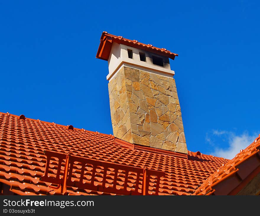 Red ceramic roof. Blue sky background. Flue fased by stone. Snow shield