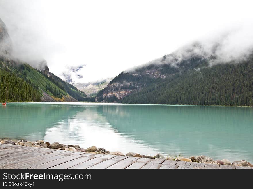 The beautiful turquoise colored Lake Louis against the backdrop of the majestic mountains of the Canadian Rockies partially covered with fog. The beautiful turquoise colored Lake Louis against the backdrop of the majestic mountains of the Canadian Rockies partially covered with fog