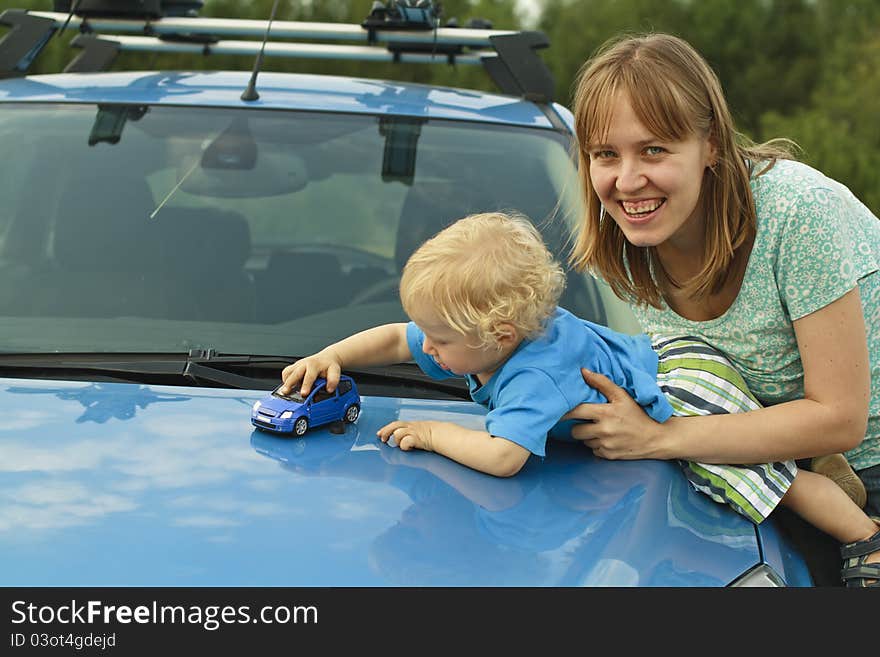 Baby playing car toy on hood with mother