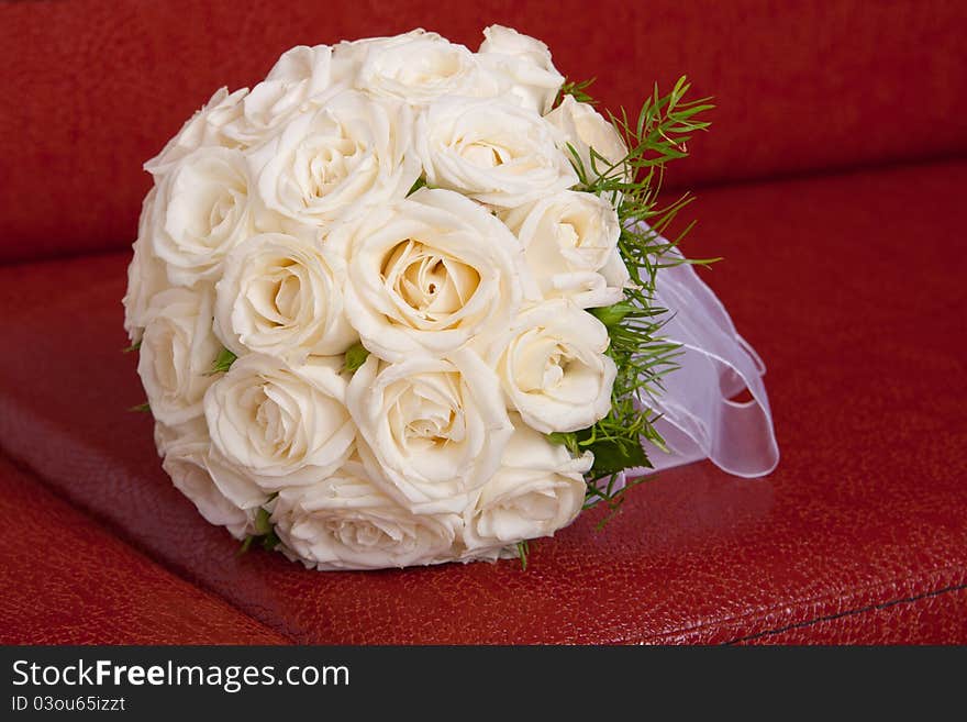 Wedding bridal bouquet of white roses lay on a red couch