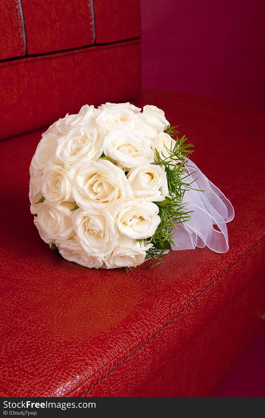 Wedding bridal bouquet of white roses lay on a red couch