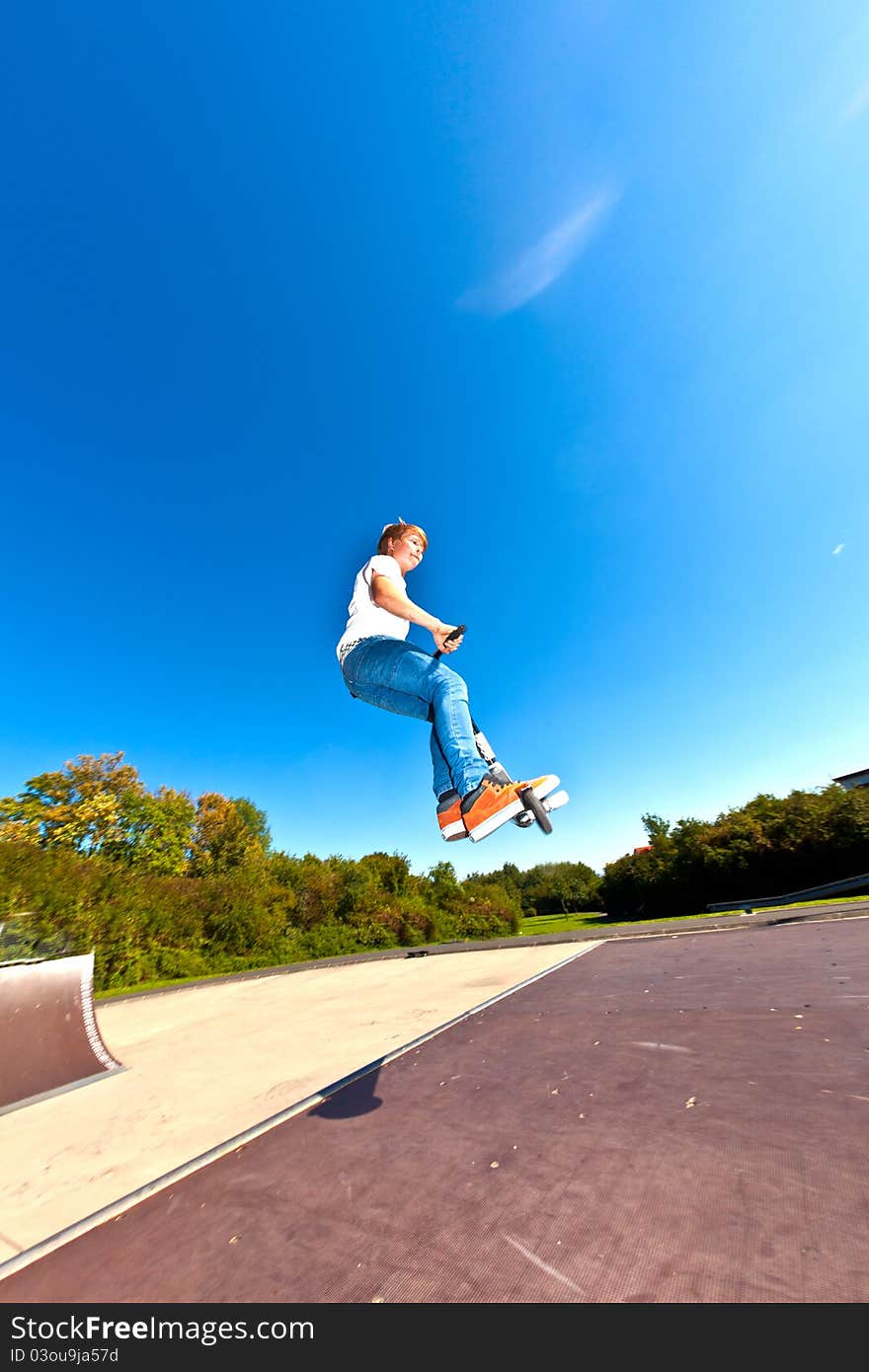 Boy jumping with his scooter at the skatepark