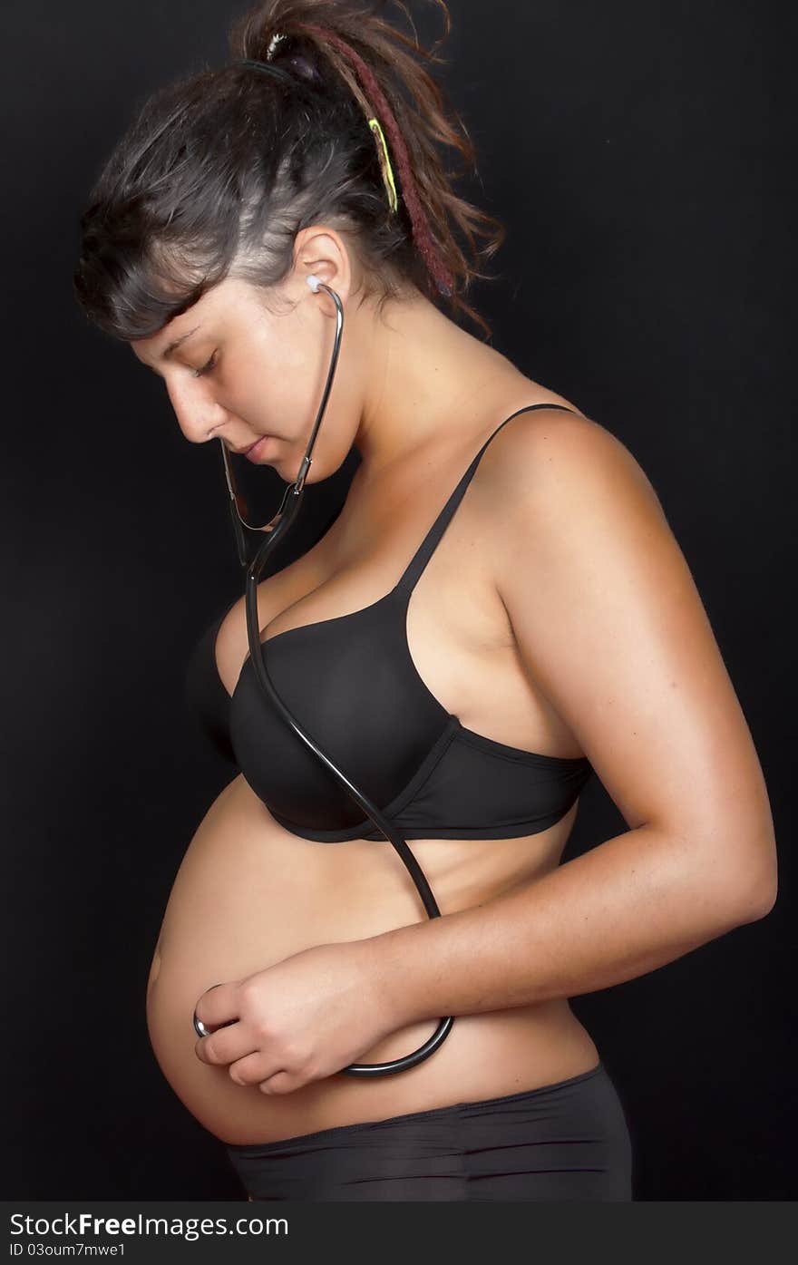 Pregnant woman with stethoscope listening to her belly isolated in black