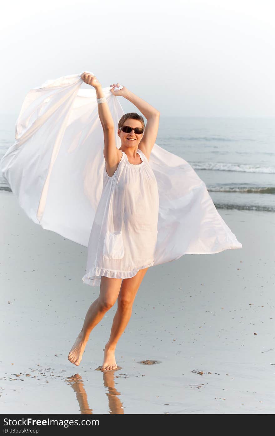 Woman is running on the beach with white shawl