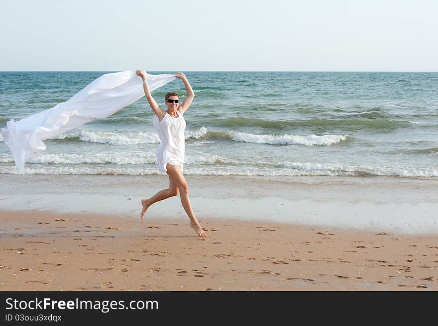 Woman is running on the beach with white shawl