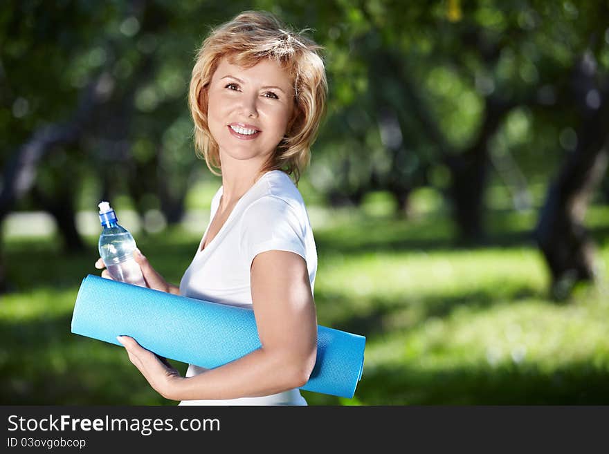 Mature woman with a gym mat and a bottle of water in the park. Mature woman with a gym mat and a bottle of water in the park