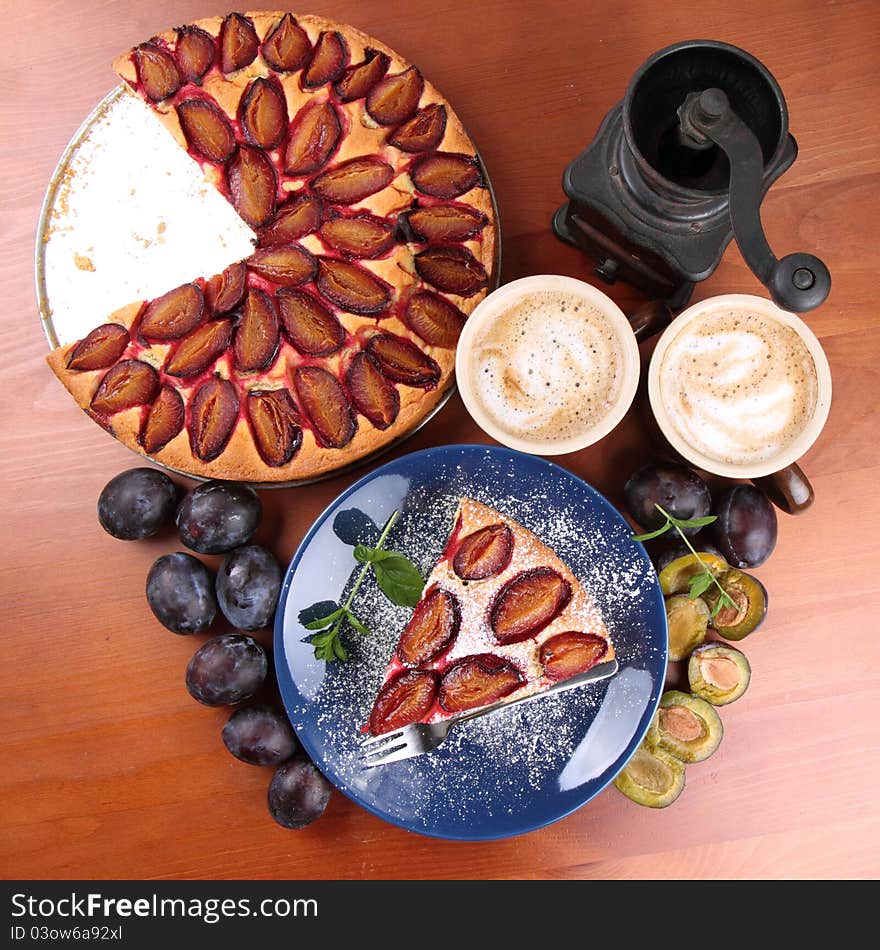 Plum pie, coffee, coffee grinder and plums decorated with mint on a wooden background. Plum pie, coffee, coffee grinder and plums decorated with mint on a wooden background