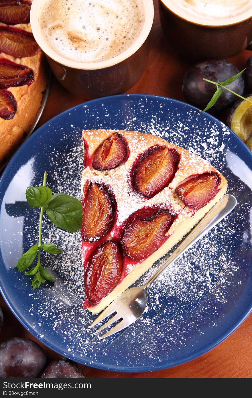 Plum pie, coffee and plums decorated with mint on a wooden background