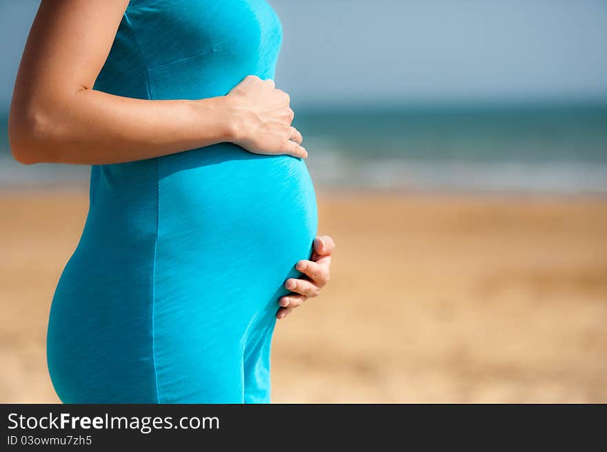 Woman is holding pregnant belly on the beach