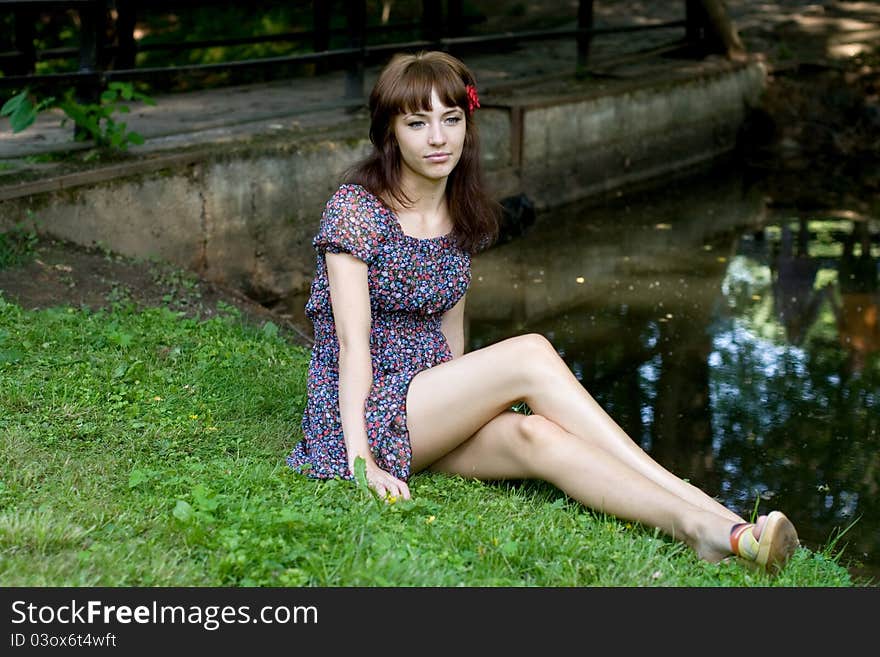 Beautiful girl sitting on bank of a river in summer