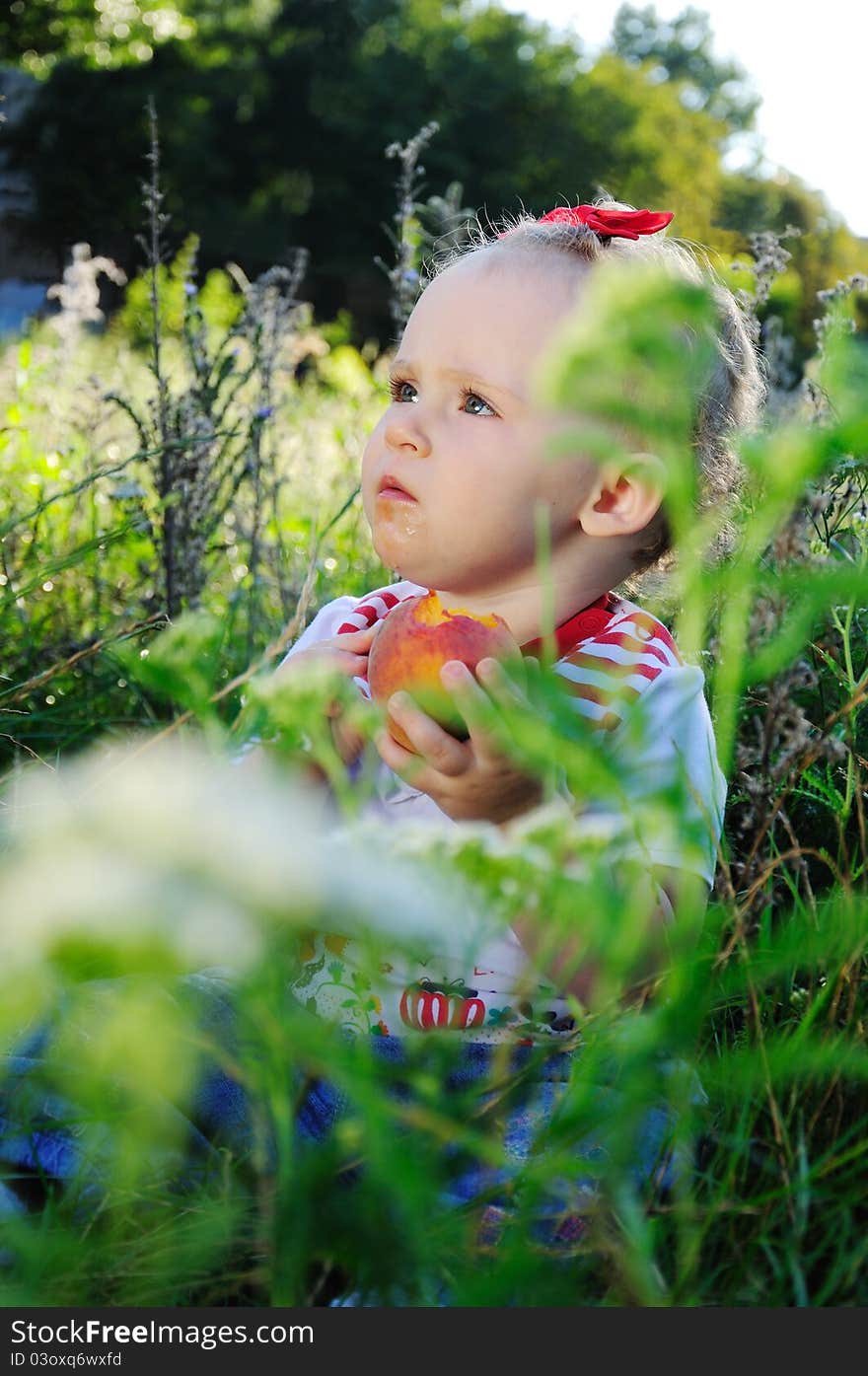 Little girl with red bow eat peach on the meadow in summer day. Little girl with red bow eat peach on the meadow in summer day