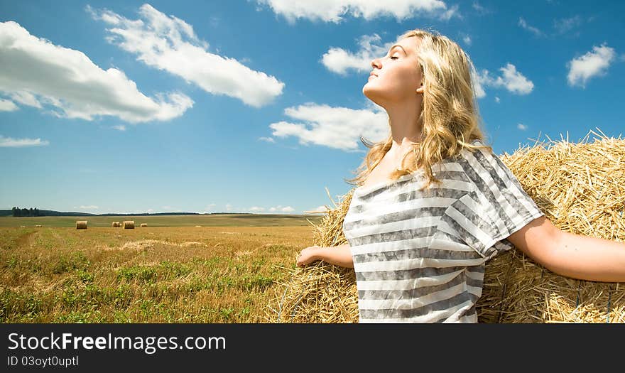 Girl at a stack of straw against a field and the sky