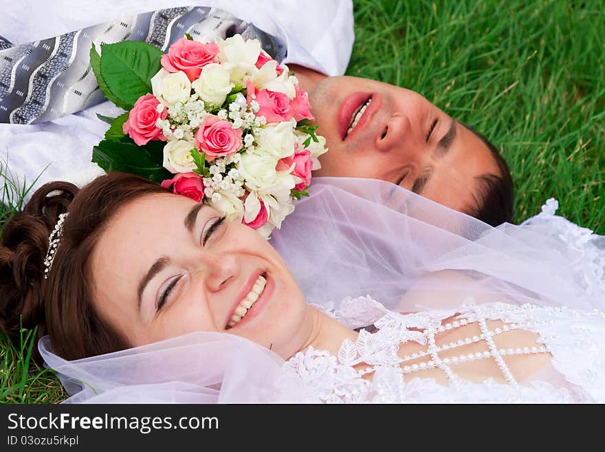 Happy bride and groom lying on a green grass