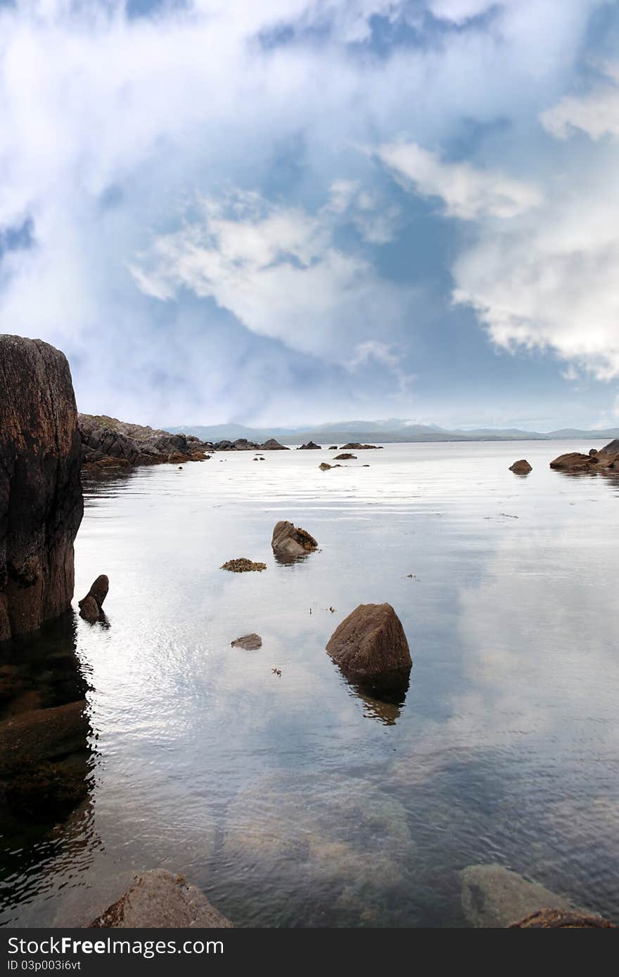 Scenic view in kerry ireland of rocks and sea with mountains against a beautiful blue cloudy sky. Scenic view in kerry ireland of rocks and sea with mountains against a beautiful blue cloudy sky