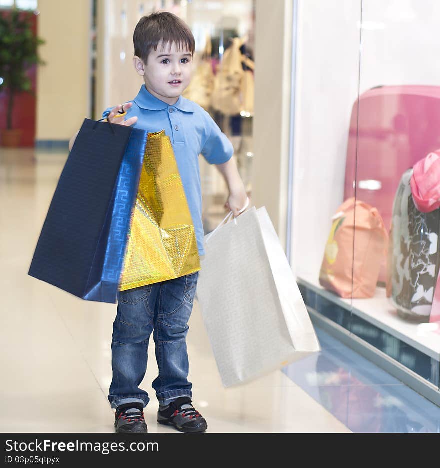 The child bears packages with purchases in shopping center. The child bears packages with purchases in shopping center