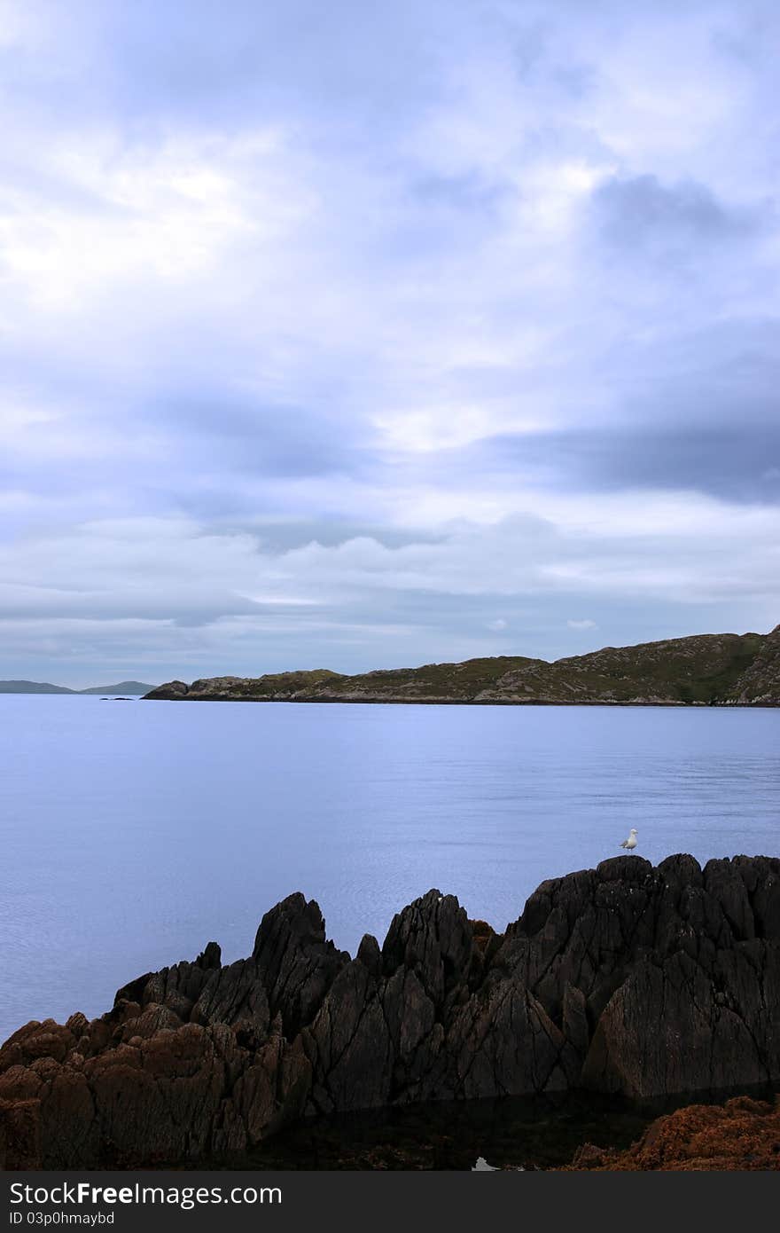 Scenic view in kerry ireland of bird on rocks and sea with mountains against a beautiful blue cloudy sky. Scenic view in kerry ireland of bird on rocks and sea with mountains against a beautiful blue cloudy sky