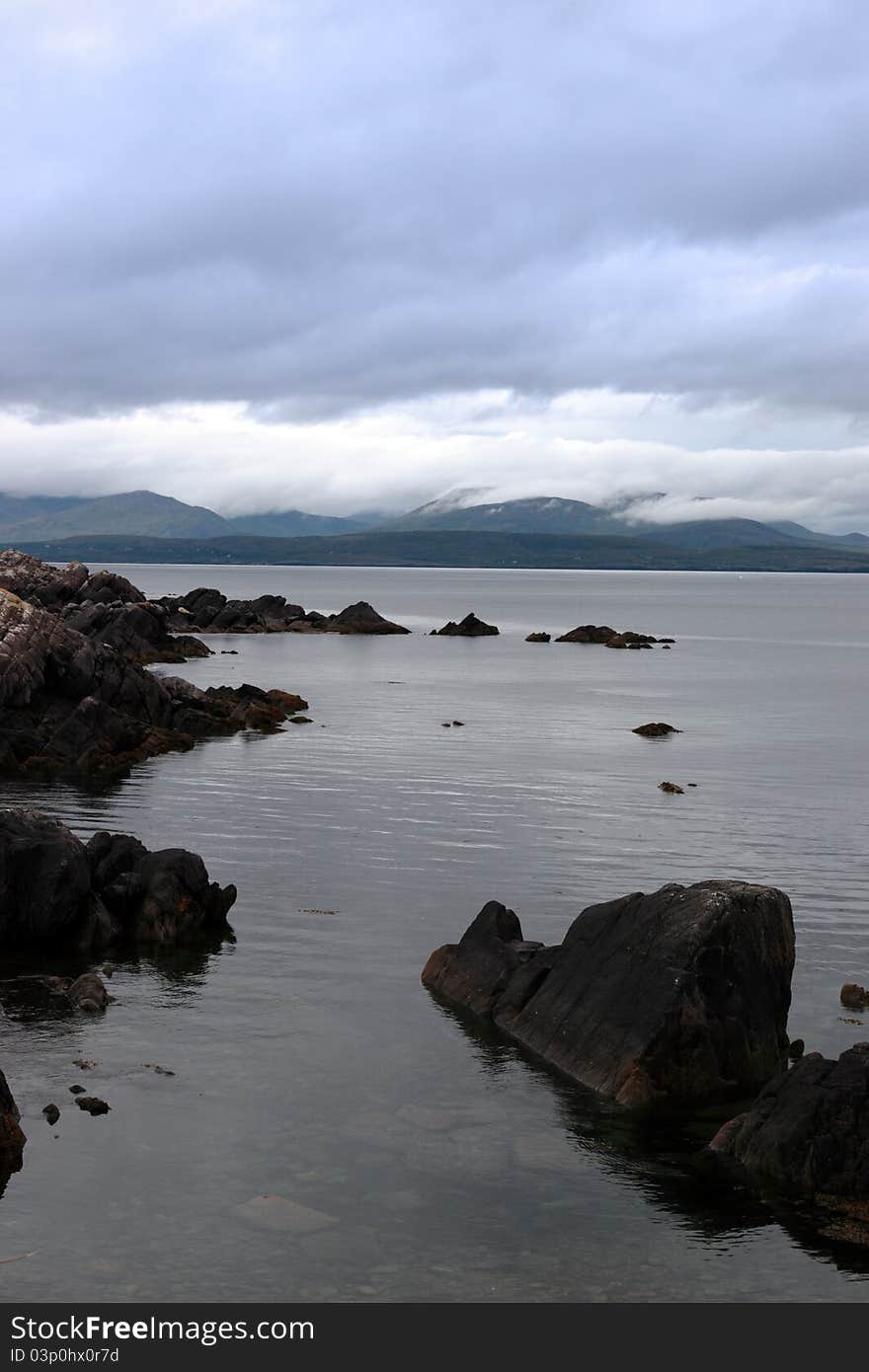 Scenic view in kerry ireland of rocks and sea with mountains against a beautiful blue cloudy sky. Scenic view in kerry ireland of rocks and sea with mountains against a beautiful blue cloudy sky