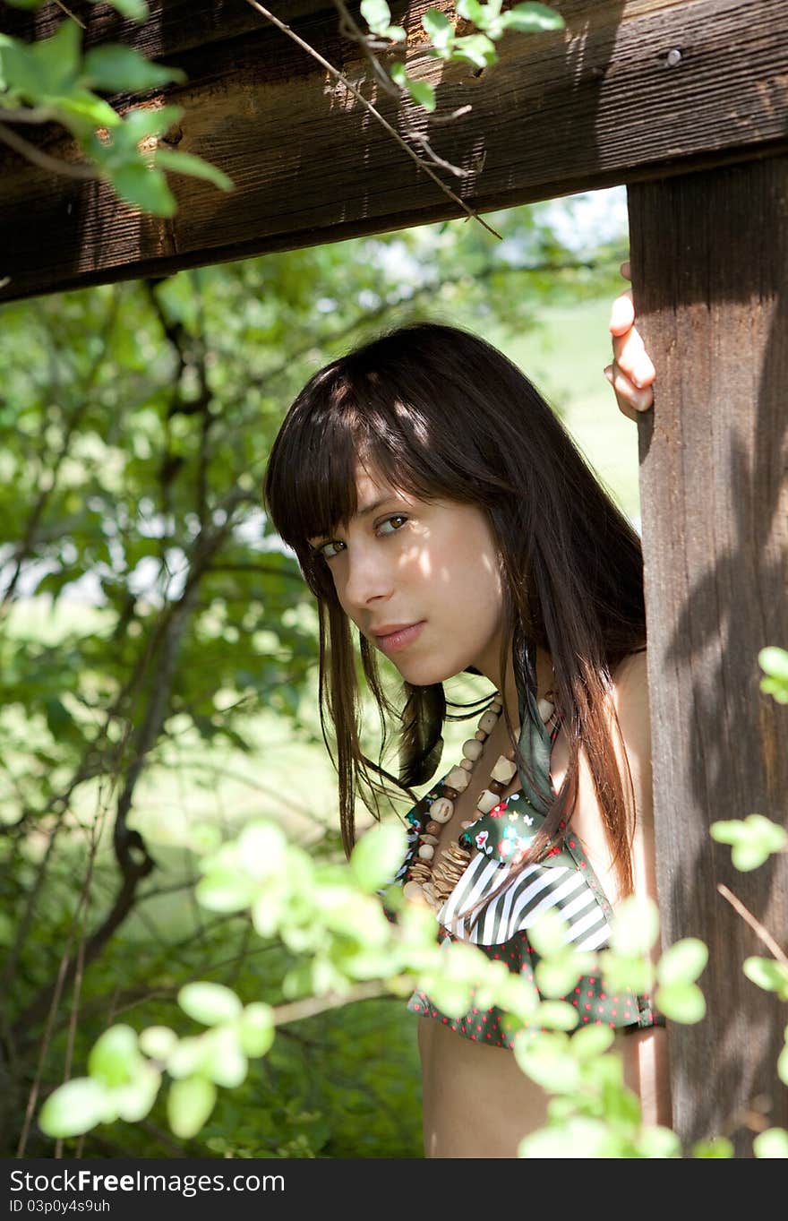 A portrait of a beautiful woman, leaning on a wooden structure and surrounded by trees. A portrait of a beautiful woman, leaning on a wooden structure and surrounded by trees