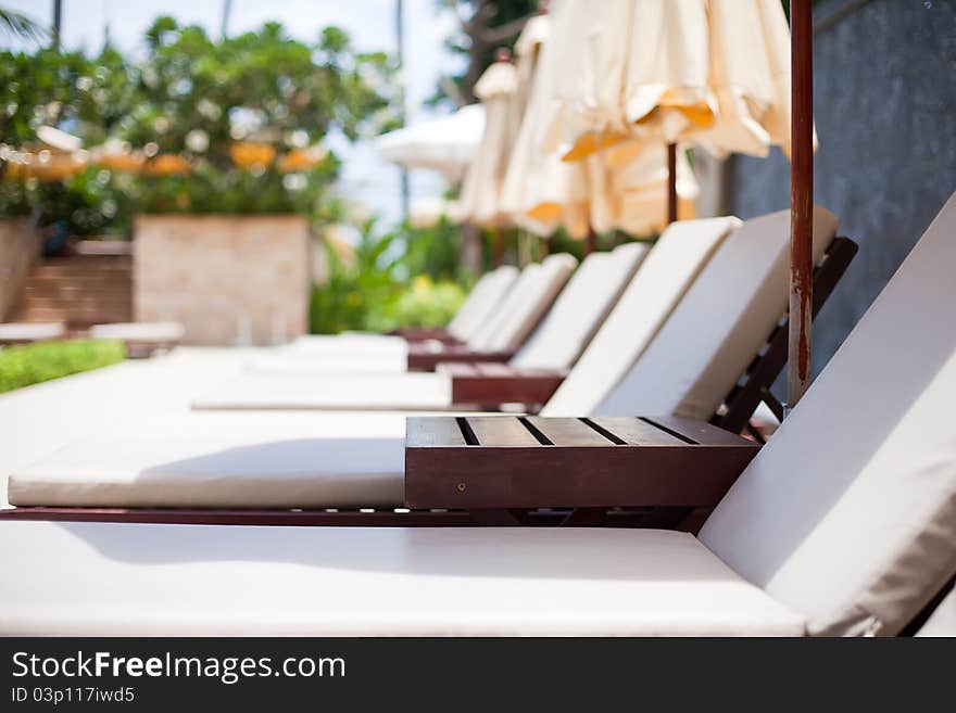 Many white plank beds with umbrellas under a shining sun. Against palm trees. Many white plank beds with umbrellas under a shining sun. Against palm trees