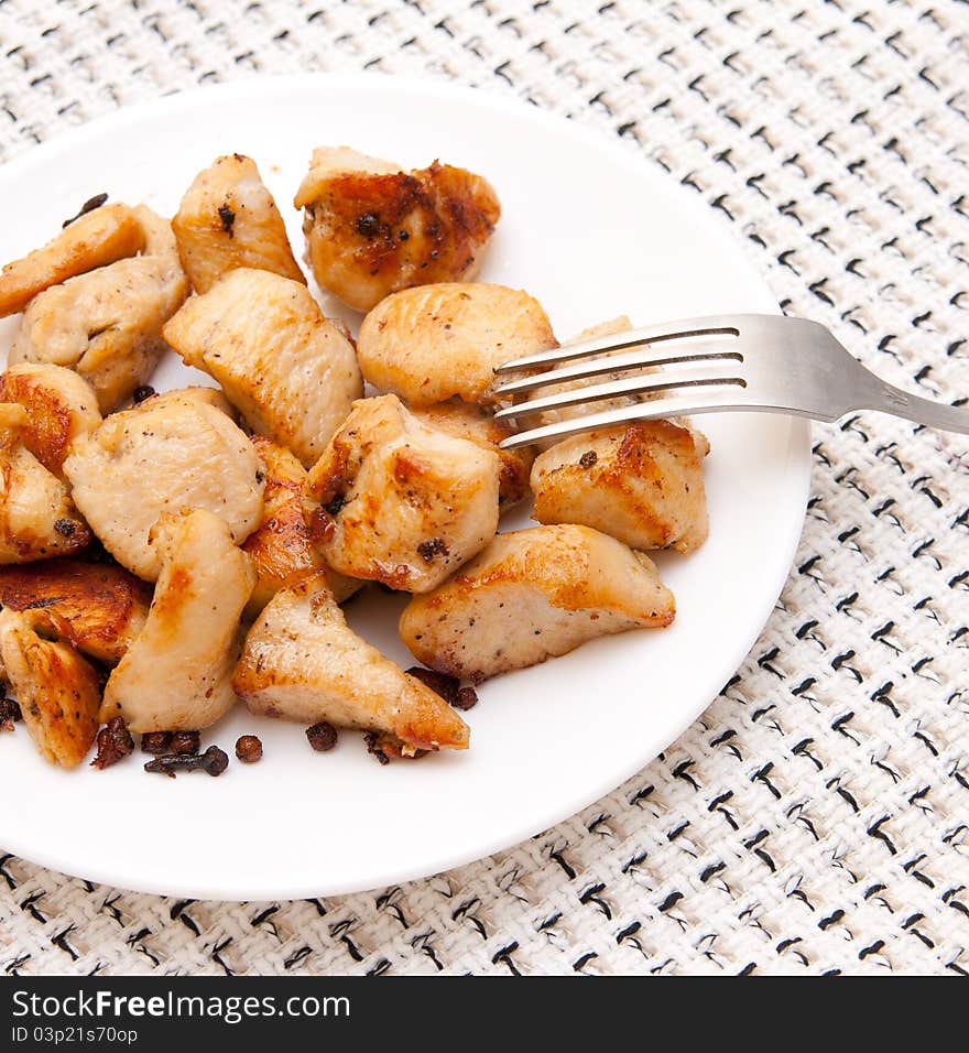 Many pieces of fried chicken well on a white plate with a fork on a checkered tablecloth. Many pieces of fried chicken well on a white plate with a fork on a checkered tablecloth