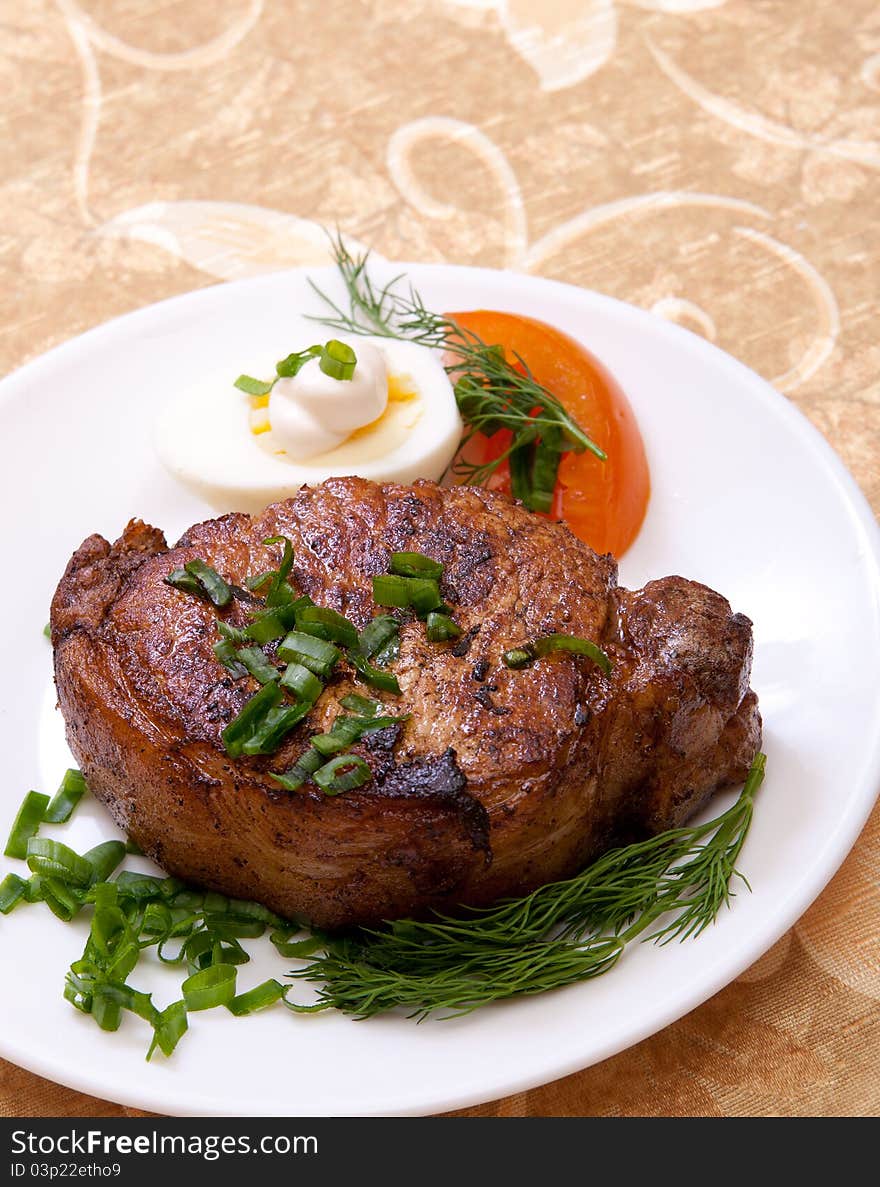 Big juicy well-done piece of meat lying on a white plate decorated with greenery. Big juicy well-done piece of meat lying on a white plate decorated with greenery