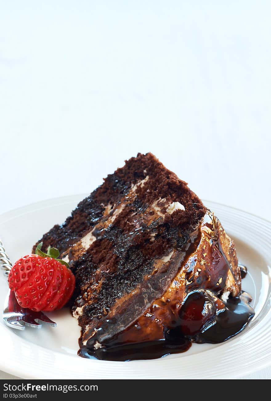 Slice of Black Forest cake with fresh cream and cherries, served on a white plate with silver fork and strawberry