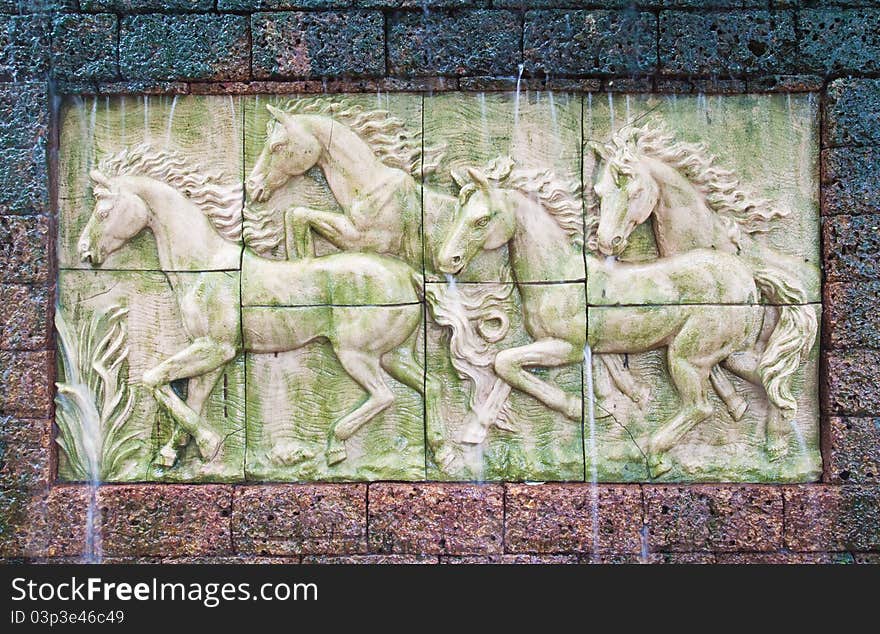 Horses in low relief statue cut out as jig saw image and water fall in front of.