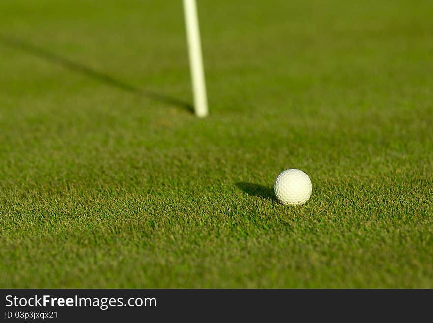 A golf ball near a hole with golf pole