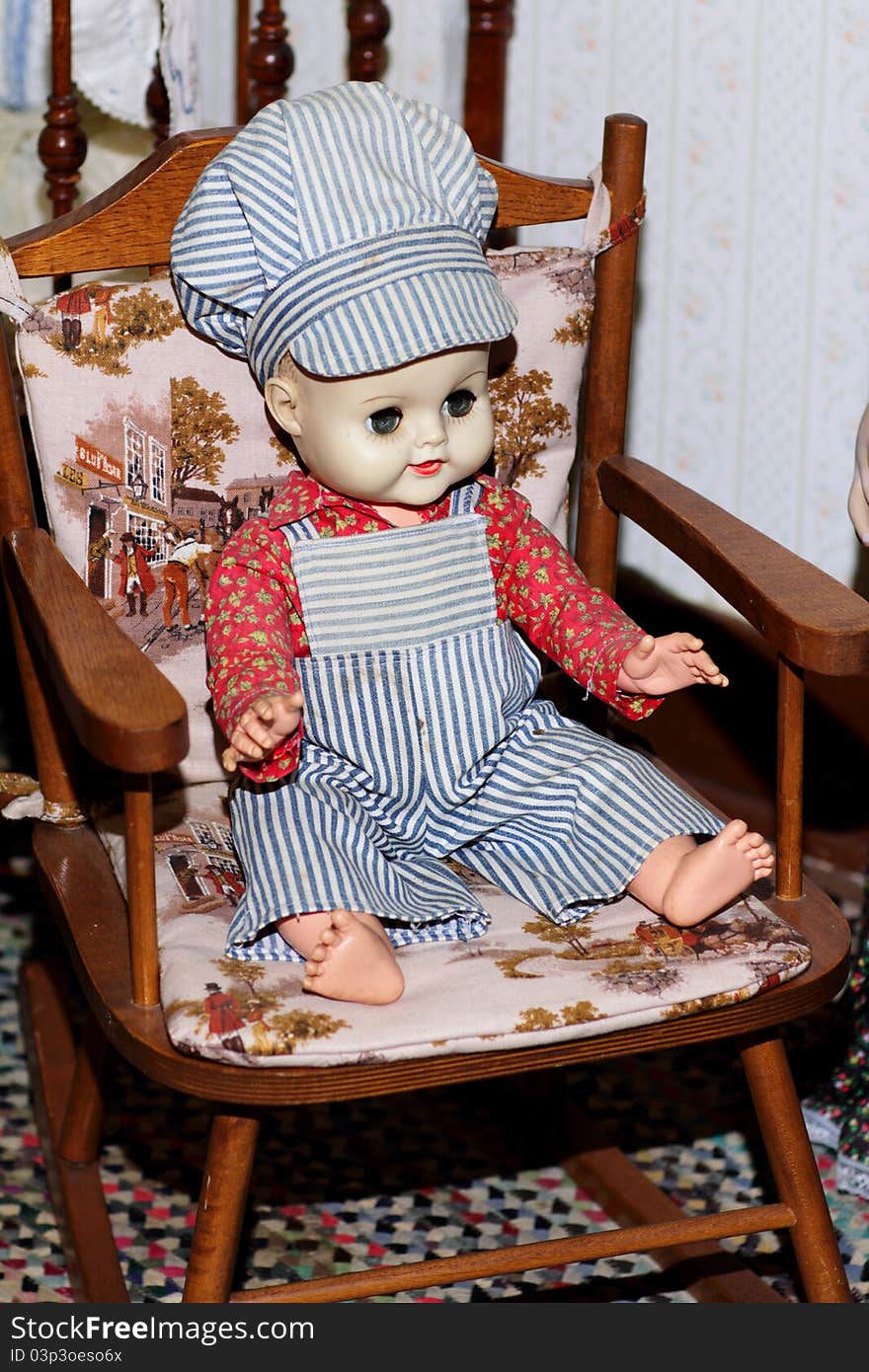 A child's old antique engineer boy doll sitting in a child's rocking chair. Shallow depth of field. A child's old antique engineer boy doll sitting in a child's rocking chair. Shallow depth of field.