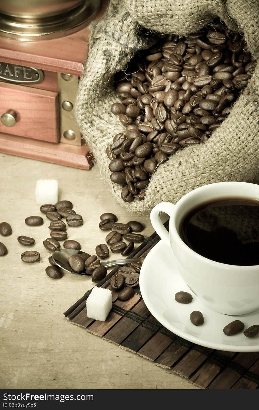 Cup of coffee and grinder with roasted beans on wooden background