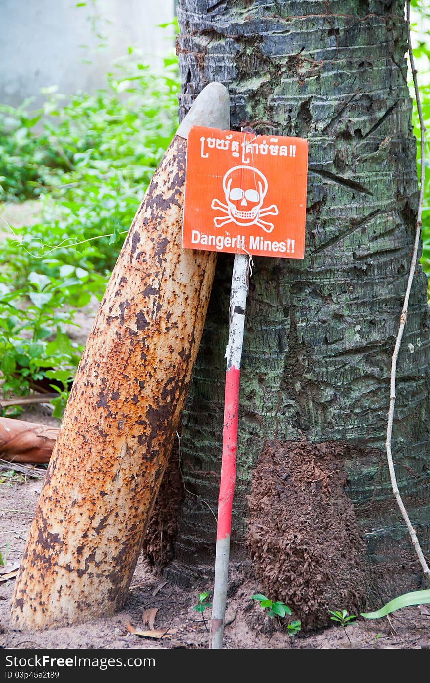 Unexploded bomb recovered from lands in Cambodia and a warning sign reminding people not to leave marked paths. Unexploded bomb recovered from lands in Cambodia and a warning sign reminding people not to leave marked paths.