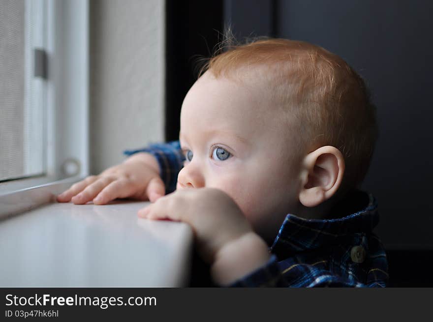 Red headed child boy with blue eyes looking out window. Red headed child boy with blue eyes looking out window.