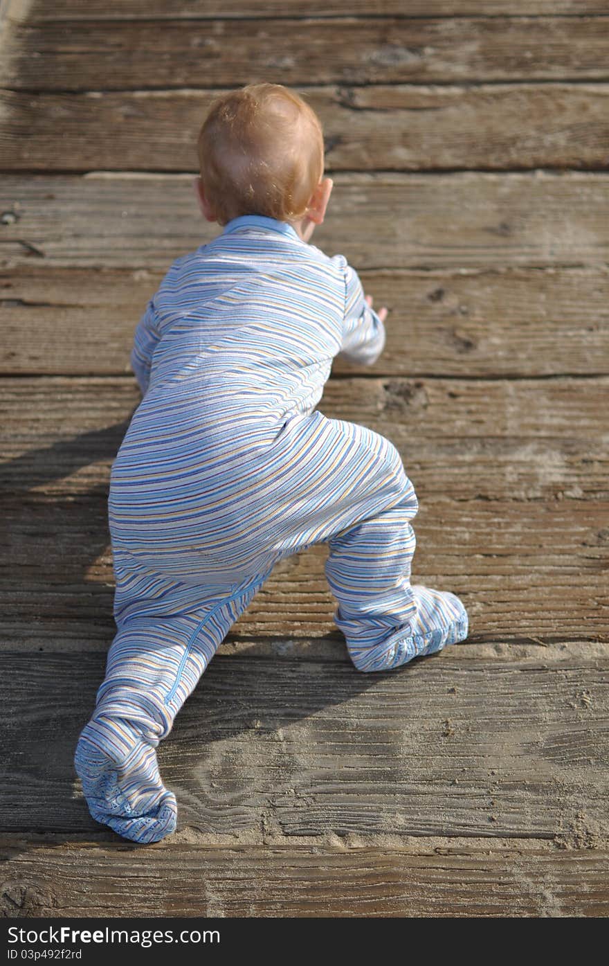 A child with strawberry blond hair wearing pajamas crawling on a wooden dock at the beach. A child with strawberry blond hair wearing pajamas crawling on a wooden dock at the beach.