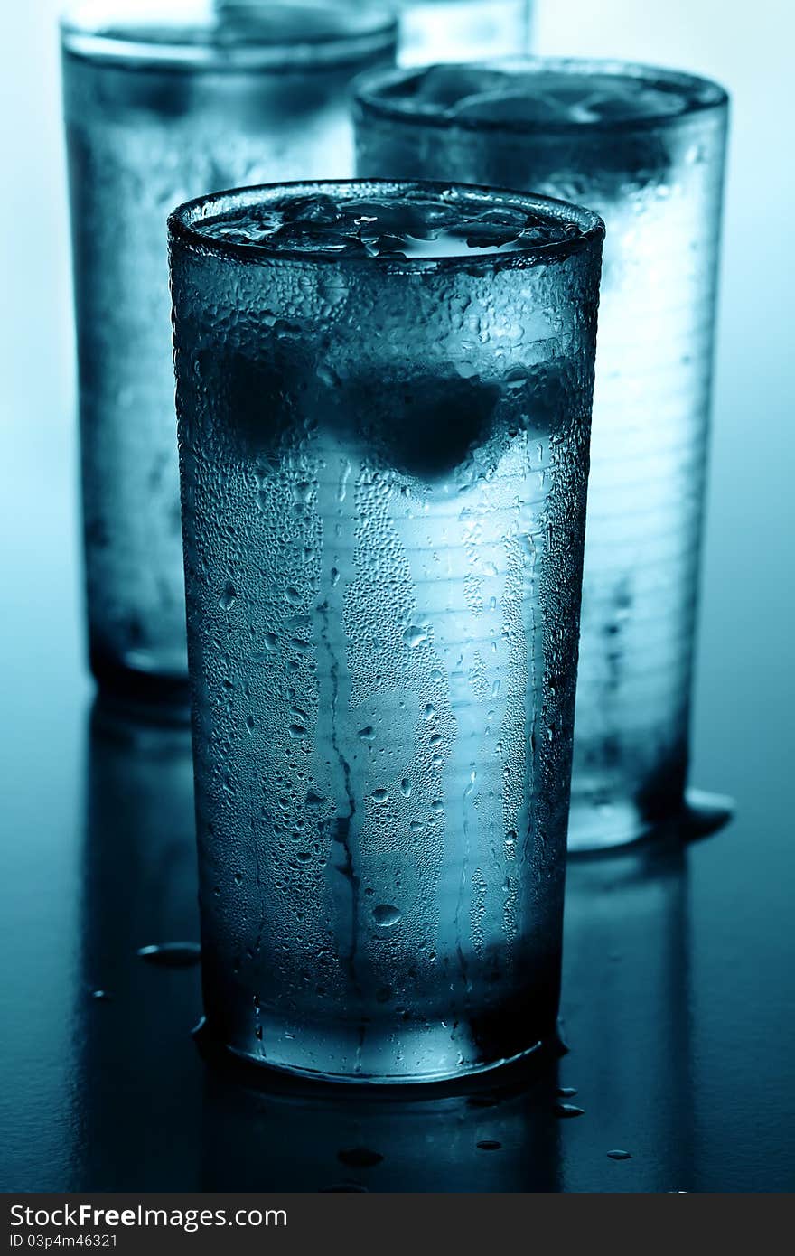 Glasses of cold water with ice cubes reflected on wet background