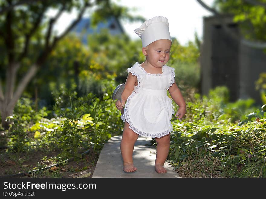 Cute little cook with big spoon goes to make dinner in the garden.