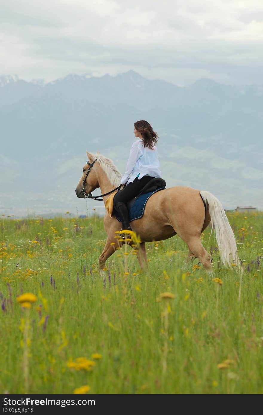 The girl skips on a green field on the horse