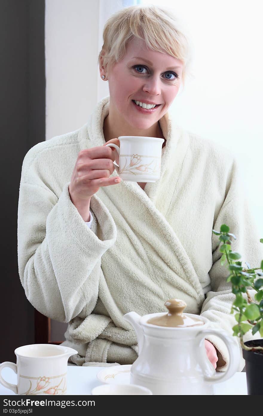 Image of a woman at home in the morning having breakfast sitting by the window having tea