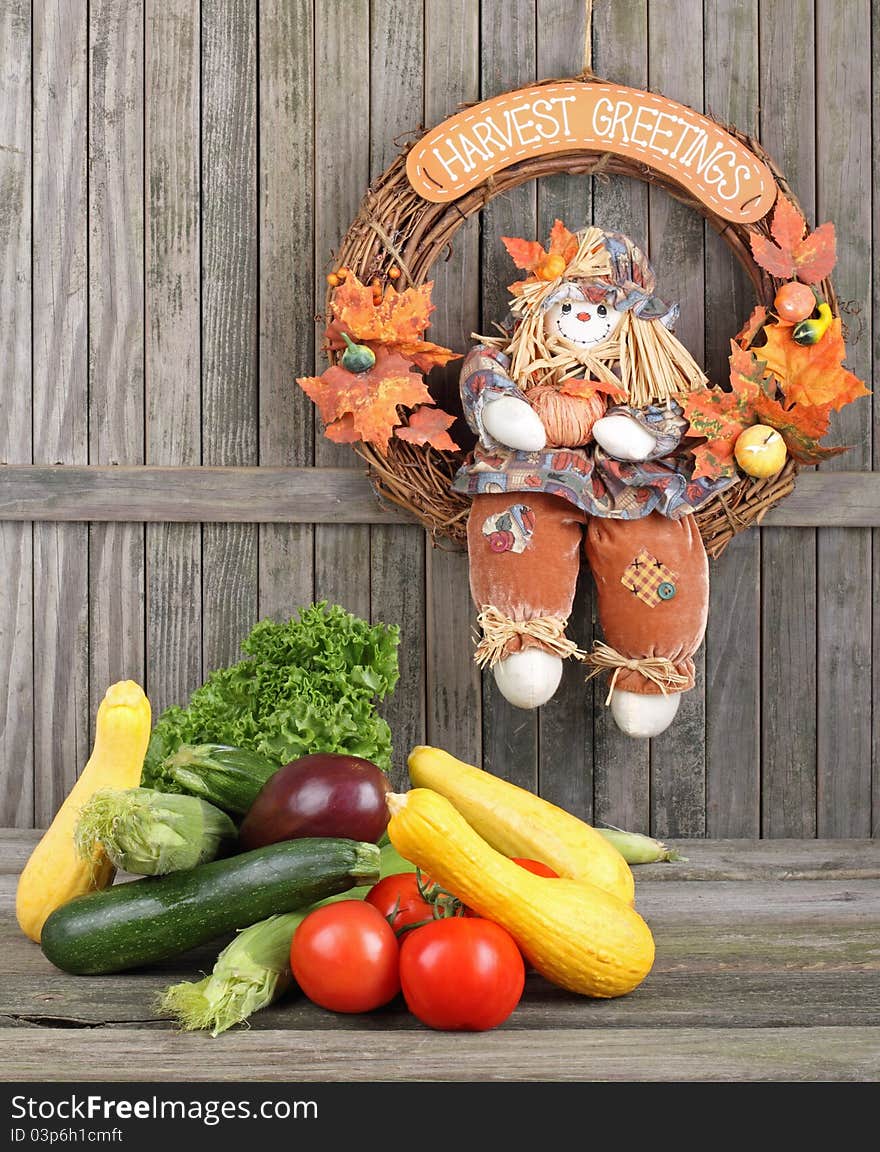 Harvested vegetables and fruits with a harvest wreath hanging on a weathered fence. Harvested vegetables and fruits with a harvest wreath hanging on a weathered fence