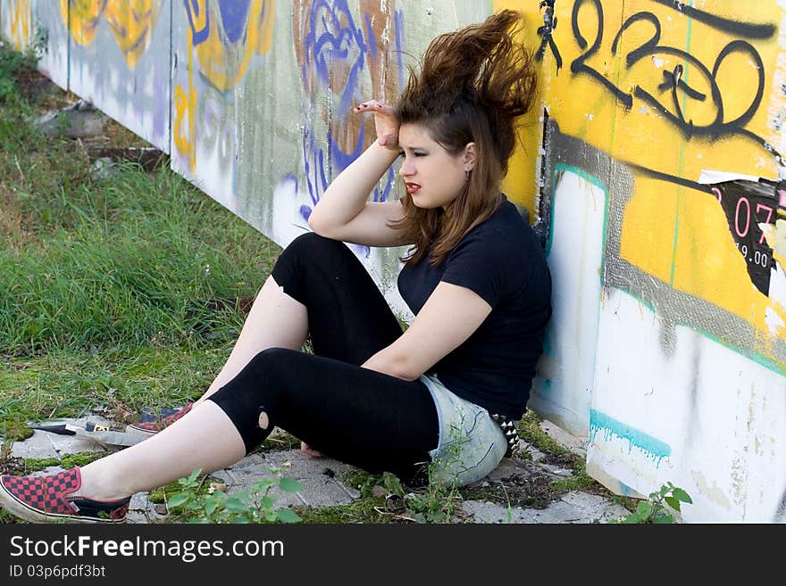 Punk girl sitting near graffiti wall